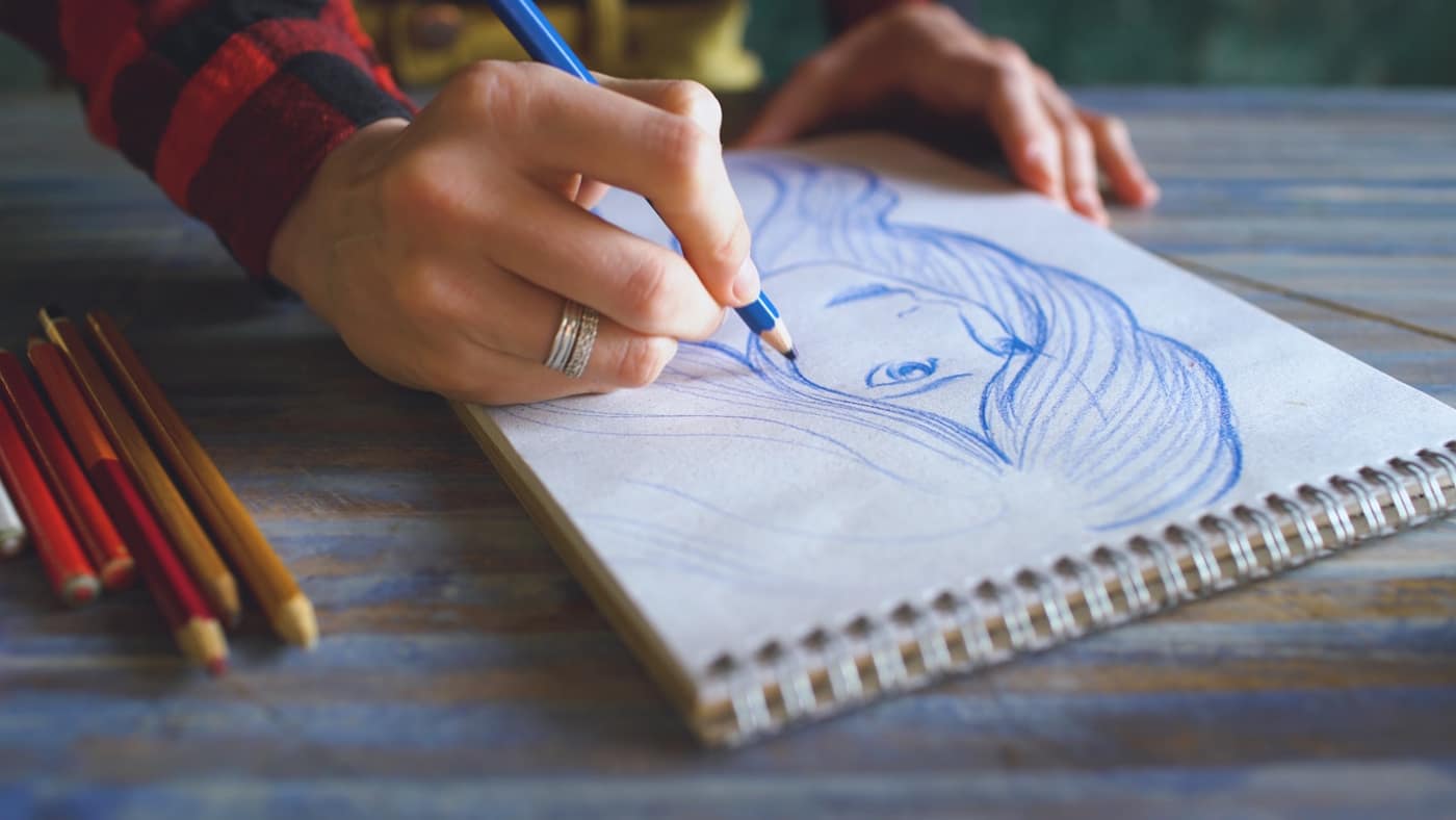 A person sketching in a sketchbook with pencils
