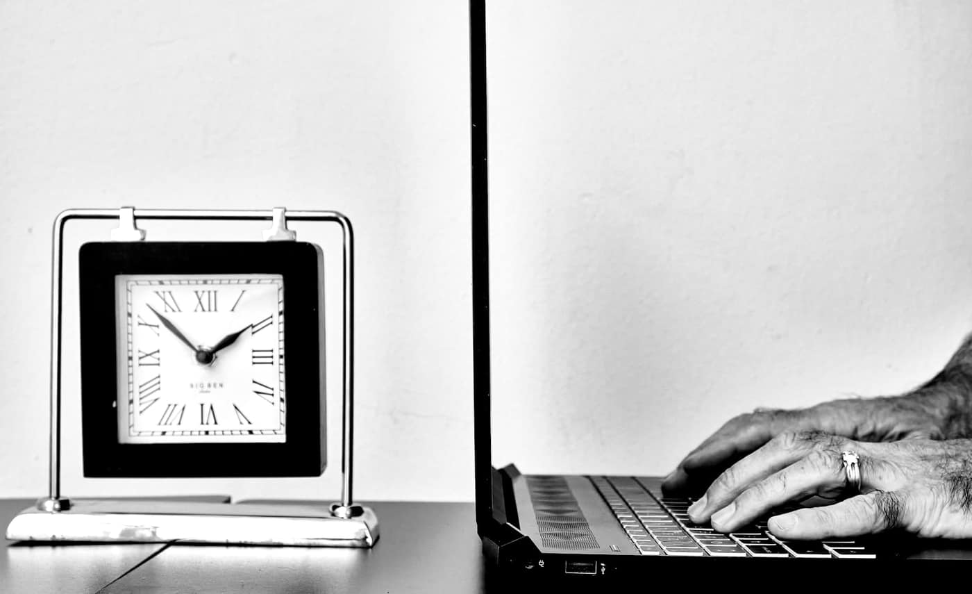 A clock and laptop on a desk for tracking work hours