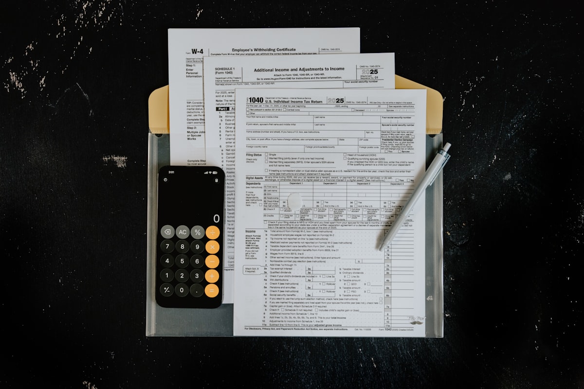 Tax forms with a calculator and pen on a dark desk surface